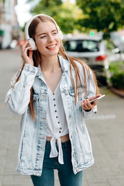 Fille heureuse tenant un smartphone et écouter de la musique dans des écouteurs en plein air