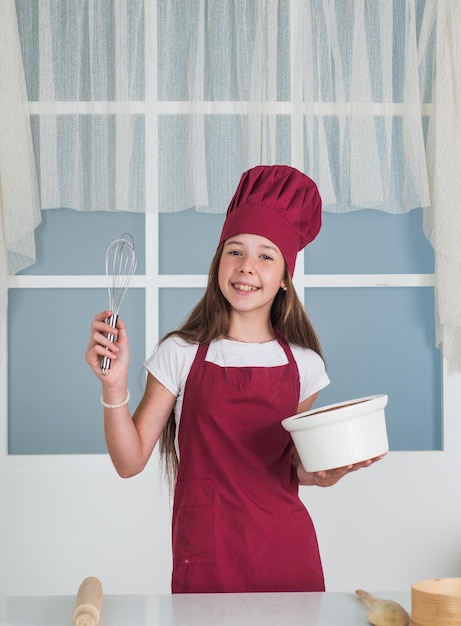 Une fille heureuse tient un bol et un batteur cuisinier