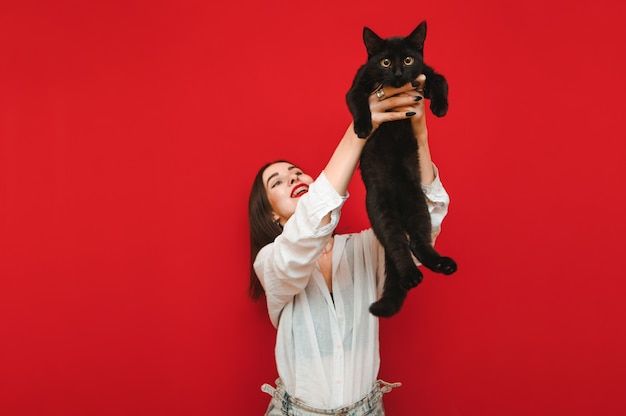 Fille heureuse tient un chat noir effrayé dans ses mains et le soulève