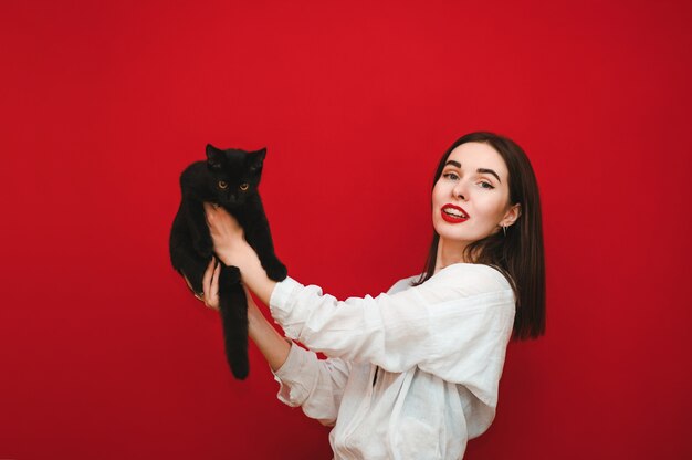 Fille heureuse tient un chat noir funky dans ses mains et le soulève