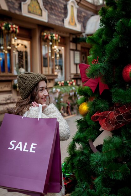 Une fille heureuse tient des sacs en papier avec le symbole de vente dans les magasins avec des ventes à Noël autour de la ville Concept de vacances shopping bonheur Ventes de Noël