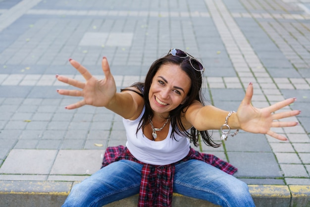 Une fille heureuse en tshirt blanc, un jean bleu et des baskets blanches est assise sur un trottoir dans un parc pendant la journée...