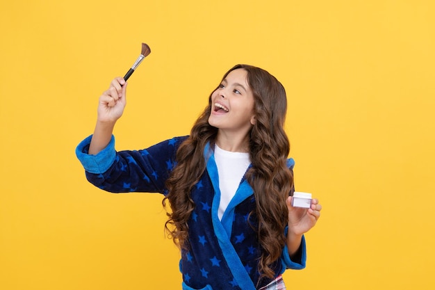 Fille heureuse en vêtements de nuit à l'aide d'un pinceau cosmétique et d'un fond de teint en poudre, soins de la peau.