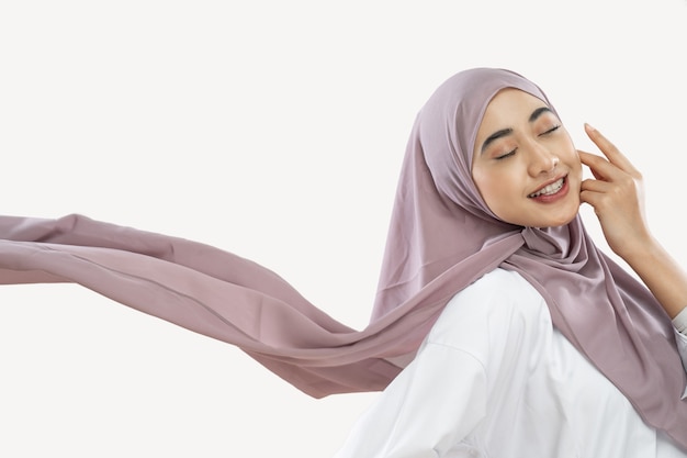 Fille hijab appréciant de porter un voile violet ondulant dans le vent avec un geste de la main sur la joue