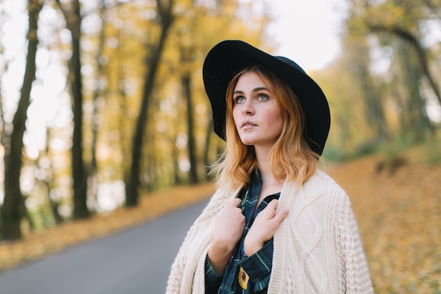 Fille hippie élégante dans un pull et un chapeau se promène dans le parc en automne.