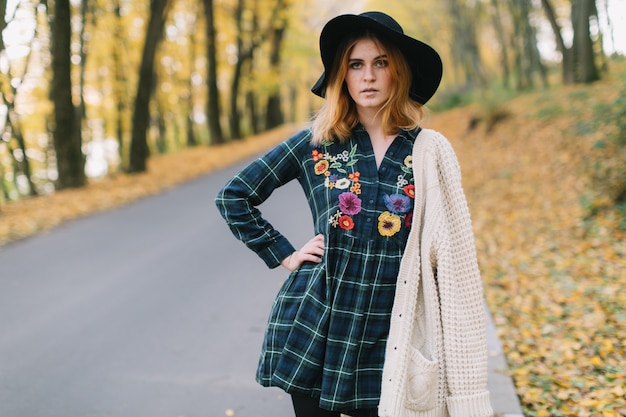 Fille hippie élégante dans un pull et un chapeau se promène dans le parc en automne.