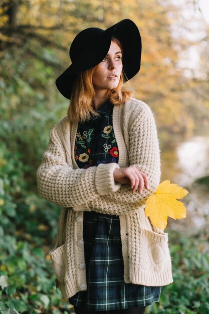 Fille hippie avec une feuille d&#39;érable jaune dans un pull et un chapeau tricotés promenades parc automne.