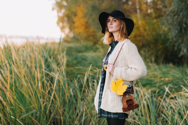 Fille hippie avec une feuille d&#39;érable jaune dans un pull et un chapeau tricotés promenades parc automne.