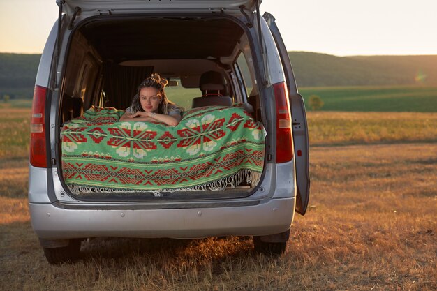 Une fille hipster est allongée dans son lit dans une camionnette sur fond de champ et le soleil couchant le ...