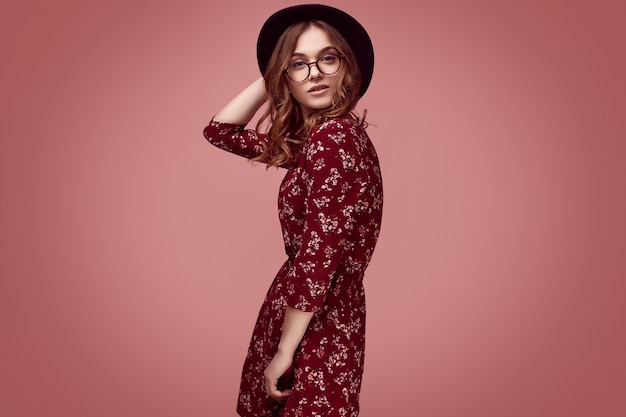 Fille de hipster glamour élégante en robe rouge, chapeau noir et lunettes