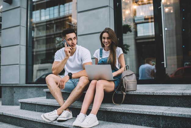 de fille hipster heureuse en vêtements assis en milieu urbain souriant à la caméra tout en charmant petit ami