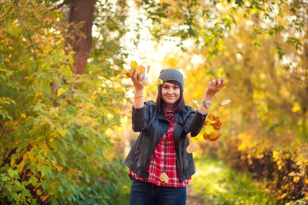 Fille hipster heureuse vomit des feuilles jaunes dans le parc d'automne