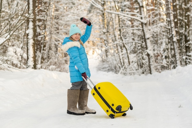 Une fille en hiver en bottes de feutre va avec une valise un jour de neige glacial