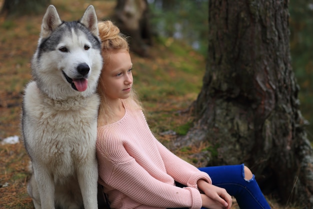 Une fille avec un husky se promène dans la forêt.