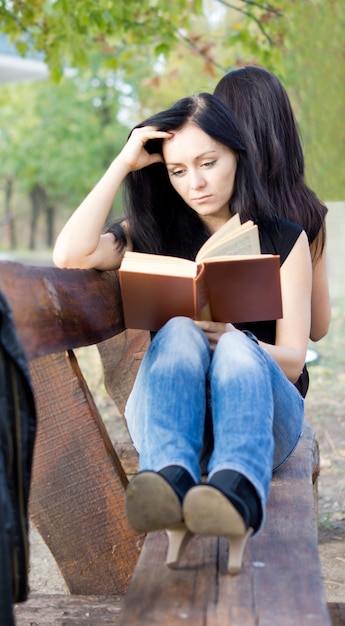 Fille immergée dans la lecture d'un livre tout en vous relaxant sur un banc de jardin en bois rustique