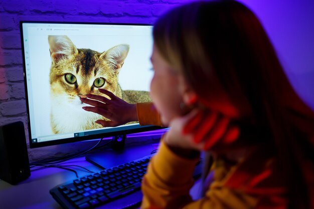 Une fille indépendante regarde un chat sur un écran d'ordinateur. Assis dans un appartement à un bureau d'ordinateur