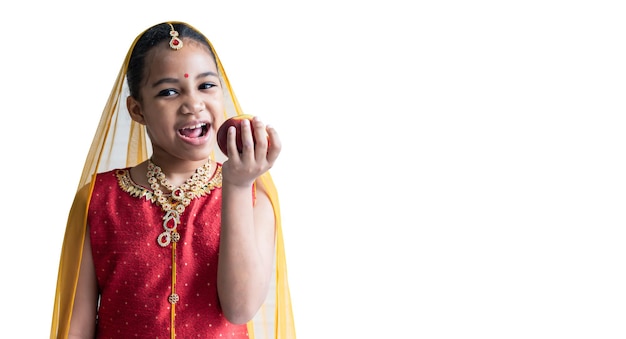 Fille indienne de 8 ans portant un sari rouge tenant et mangeant des fruits est une pomme