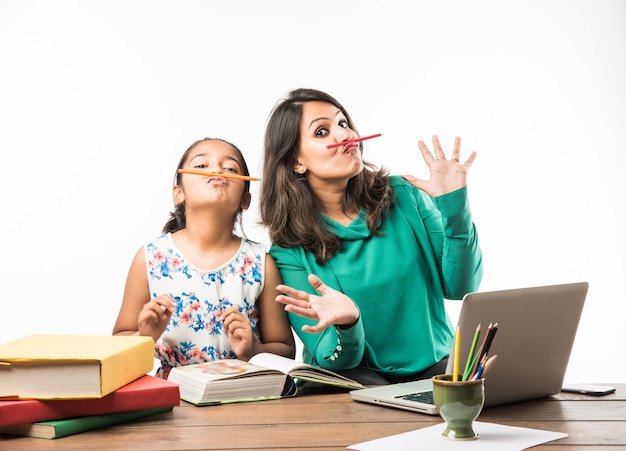 Fille indienne étudiant avec sa mère ou son enseignant à la table d'étude avec un ordinateur portable, des livres et s'amusant à apprendre