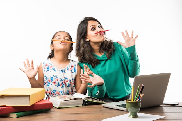 Fille indienne étudiant avec sa mère ou son enseignant à la table d'étude avec un ordinateur portable, des livres et s'amusant à apprendre