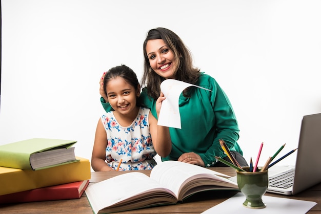 Fille indienne étudiant avec sa mère ou son enseignant à la table d'étude avec un ordinateur portable, des livres et s'amusant à apprendre