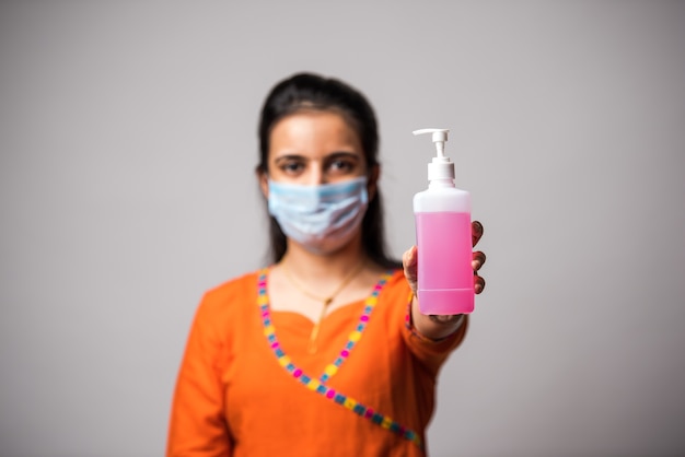 Fille indienne montrant un désinfectant pour les mains portant un masque médical. Lavage des mains antiseptique. Concept de virus corona