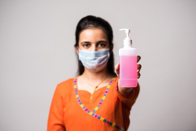 Fille indienne montrant un désinfectant pour les mains portant un masque médical. Lavage des mains antiseptique. Concept de virus corona