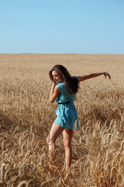 Fille insouciante dans une robe d'été bleue profite du soleil dans un champ de blé