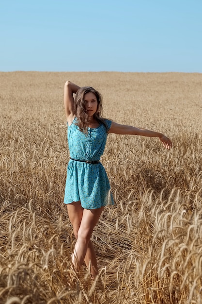 Fille insouciante dans une robe d'été bleue profite du soleil dans un champ de blé