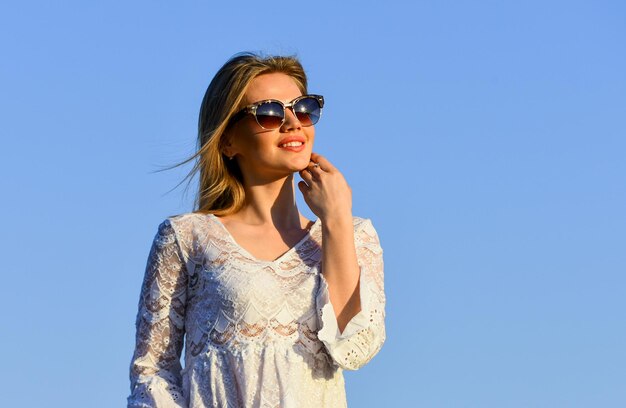 Fille insouciante Jolie femme lunettes de soleil à la mode à l'extérieur Fille robe blanche se sentir libre Loisirs et repos Été se détendre Journée ensoleillée Fille fond de ciel bleu Santé féminine Fille émotionnelle Heureuse