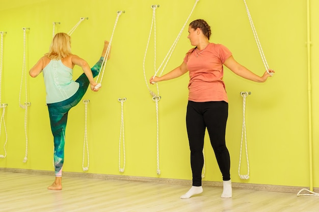Une fille avec un instructeur effectue un exercice près d'un mur jaune avec des cordes dans le gymnase
