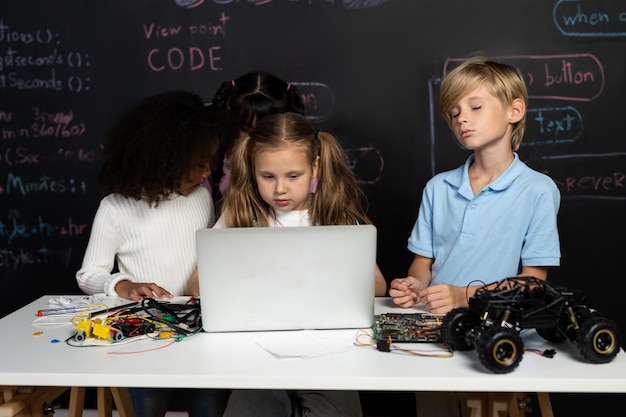 Une fille intelligente avec un bib blanc qui apprend la technologie robotique en utilisant un ordinateur portable Erudition