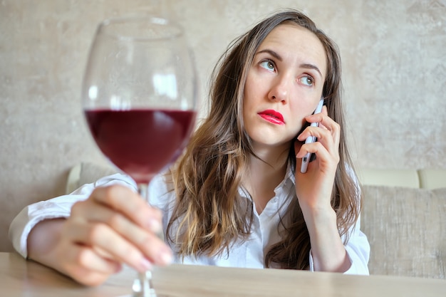 Fille ivre boit du vin et parle sur le smartphone.