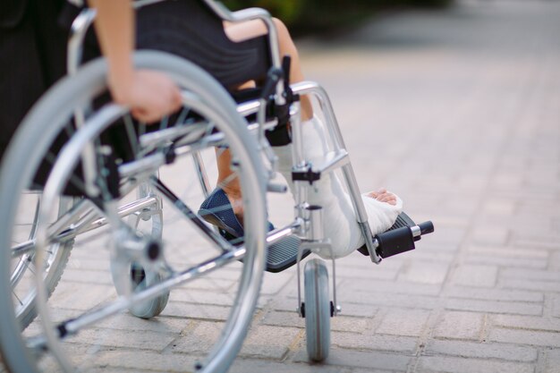 Fille avec une jambe cassée est assise dans un fauteuil roulant