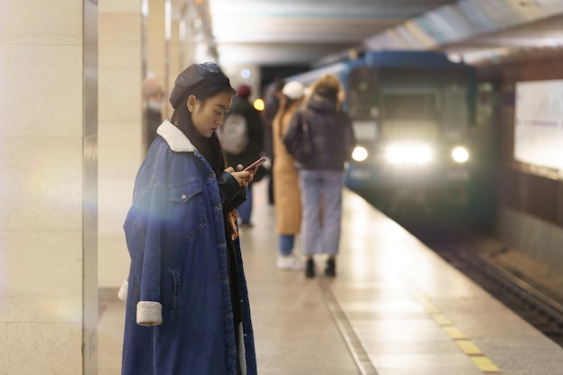 Fille japonaise occupée dans le téléphone portable à la station de métro avec le train arrivant jeune femme message à un ami