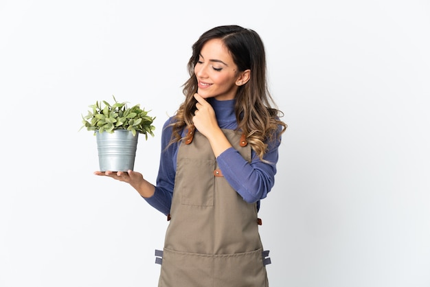 Fille de jardinier tenant une plante isolée sur fond blanc à la recherche sur le côté et souriant