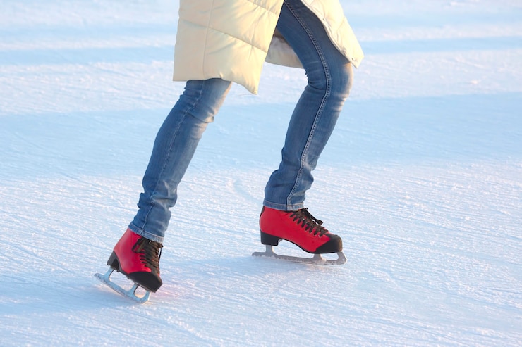 Photo fille en jean bleu patine activement sur des patins à glace rouges sur une patinoire. sport et loisirs. vacances et plaisirs d'hiver