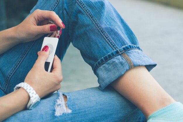 Fille en jeans assis sur le banc et connectez le casque à son lecteur de musique