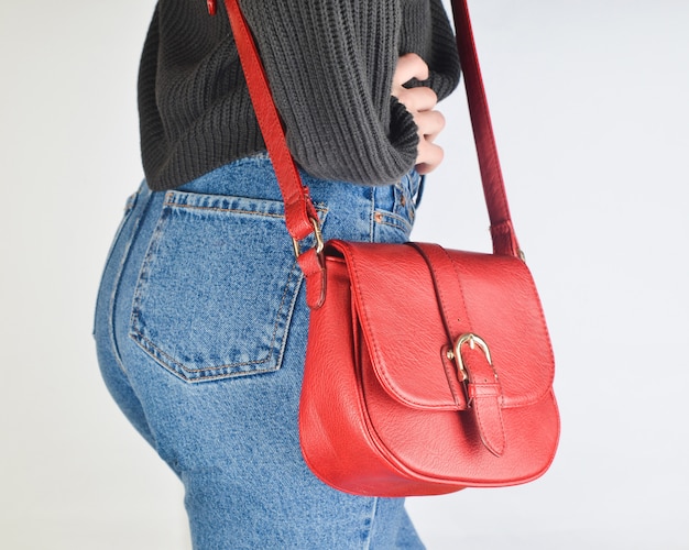 Fille en jeans fit, pull et avec sac sur les cotes posant. Vue de côté.