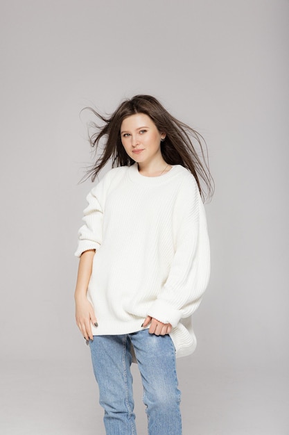 Fille en jeans légers et un pull surdimensionné blanc sur fond gris