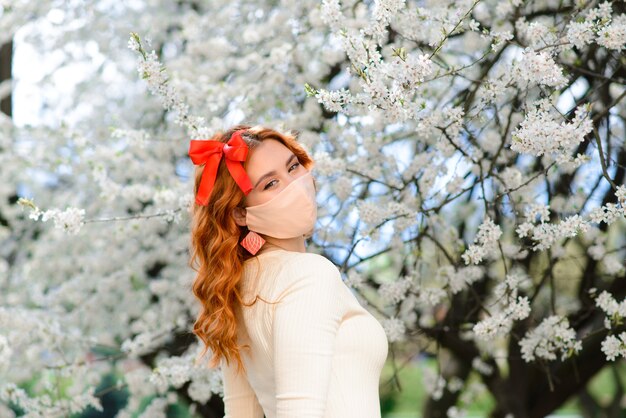 Fille, jeune femme dans un masque médical stérile protecteur sur son visage dans le jardin de printemps.