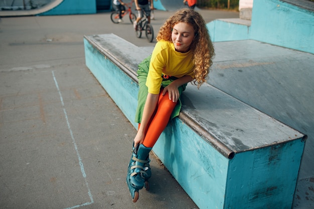 Fille de jeune femme dans des vêtements verts et jaunes va patin à roulettes.