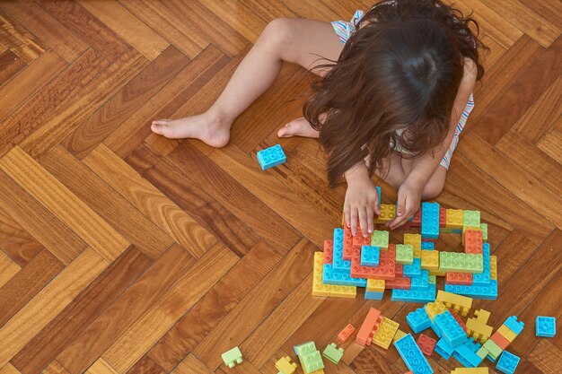 Fille jouant avec des blocs sur le plancher en bois dans sa chambre