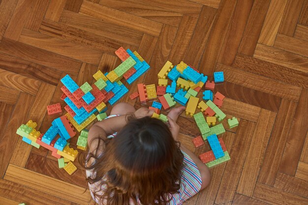 Fille jouant avec des blocs sur le plancher en bois dans sa chambre