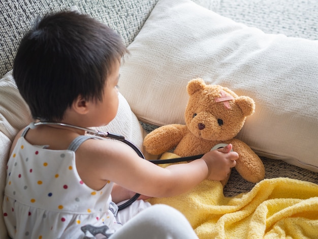 Fille joue docteur avec stéthoscope et poupée d&#39;ours