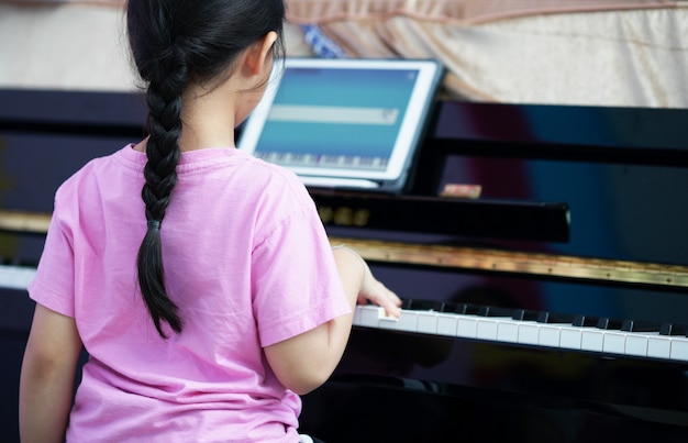 Fille joue du piano avec tablette d'apprentissage en ligne