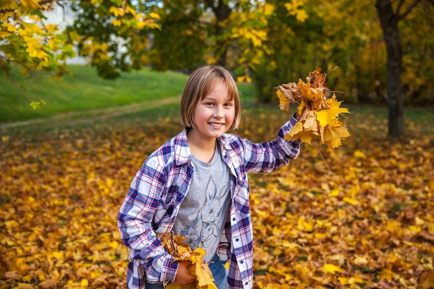 La fille joue avec les feuilles d'automne jaunes en parc