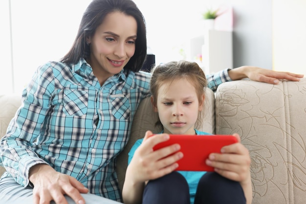 Fille joue à des jeux vidéo en ligne sur smartphone et maman le regarde