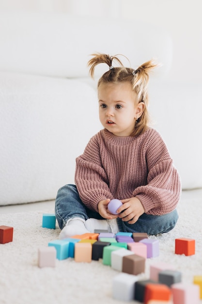 Fille joue des jouets dans le salon Jouet en bois Montessori pyramide pliée Cercle triangle rectangle éléments en bois de jouets pour enfants jouet coloré bleu jaune rouge vert