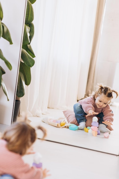 Fille joue des jouets dans le salon Jouet en bois Montessori pyramide pliée Cercle triangle rectangle éléments en bois de jouets pour enfants jouet coloré bleu jaune rouge vert