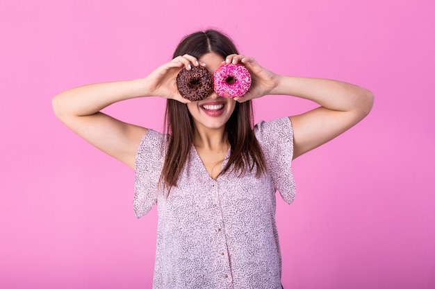 Fille joyeuse avec des beignets colorés contre ses yeux.